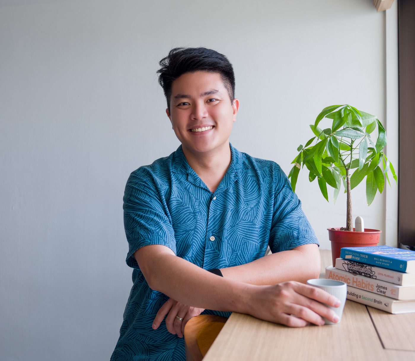 Terry Toh, smiling, leaning on a desk with a coffee mug in hand